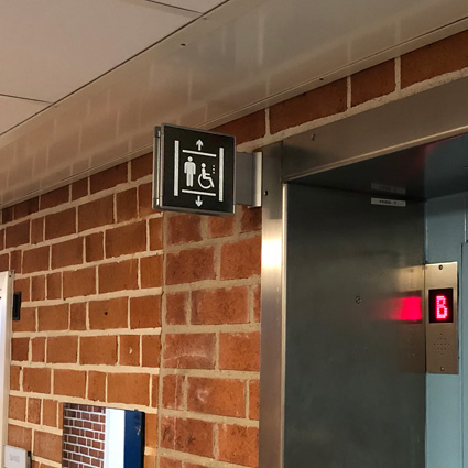 Signcode dubbelsidig flaggskylt 150x150mm utanför hiss på Elidens skola i Nacka